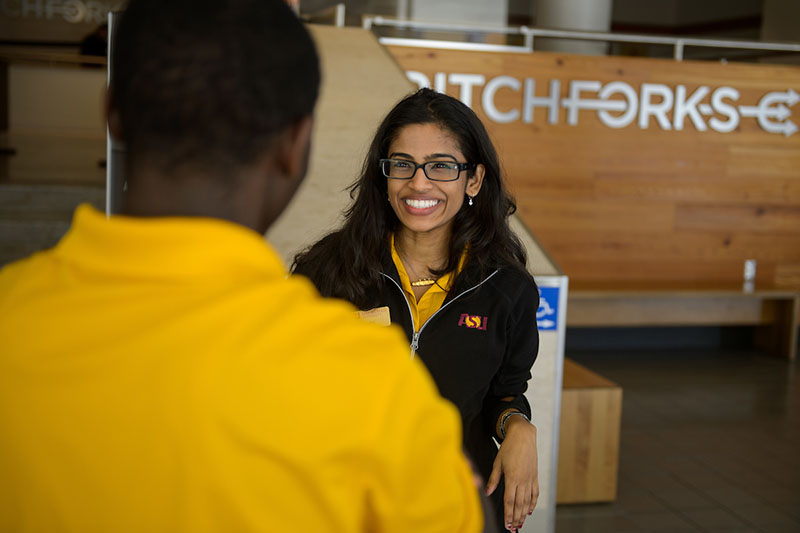 A student wearing a gold shirt talking to another student 