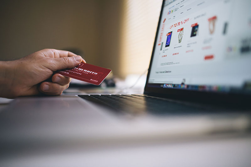 Man holding credit card next to laptop computer as if to use it for shopping