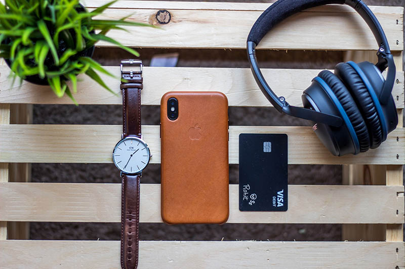 a table with a watch, iPhone, credit card and headphones