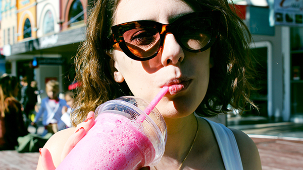 college student wearing sunglasses drinking a pink smoothie