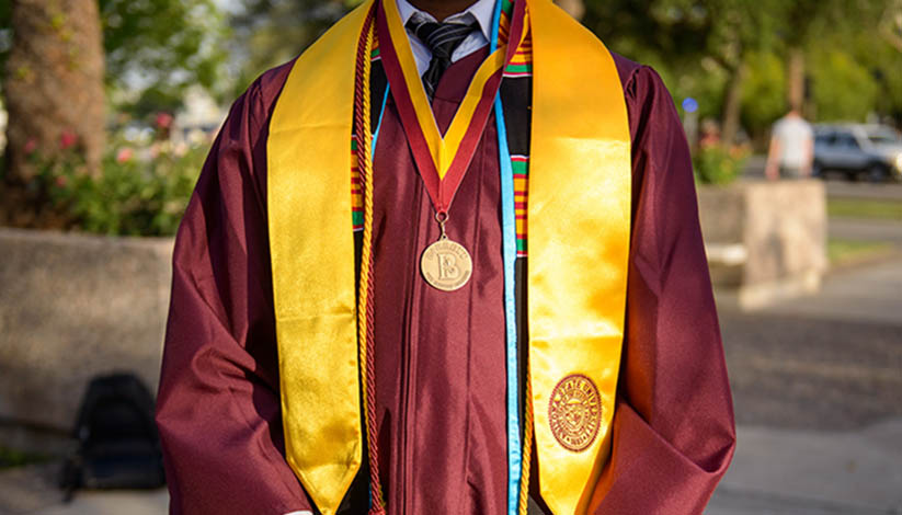 student wearing graduation robes with stole and barrett medal