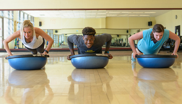 three students exercising on a bosu