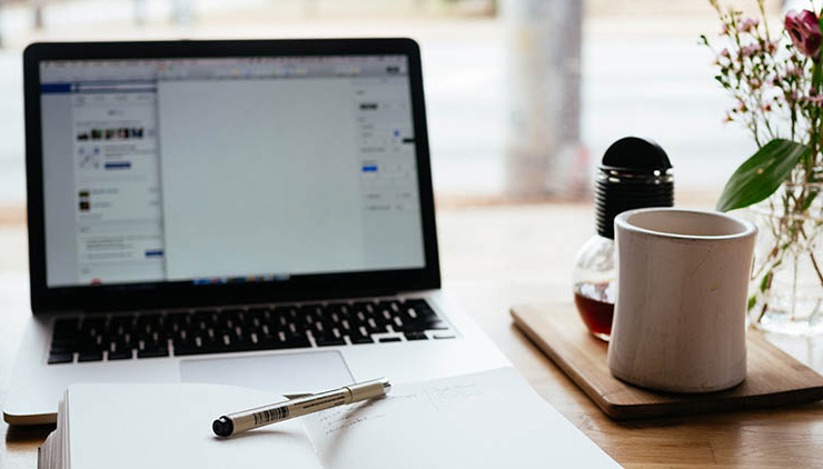 A desk with a laptop, notebook, coffee cup and plant