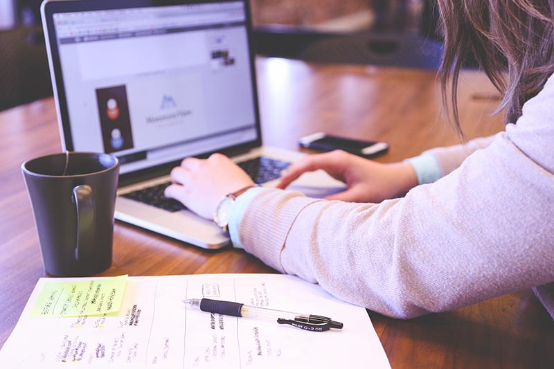 Student using computer with coffee cup on the side and notes